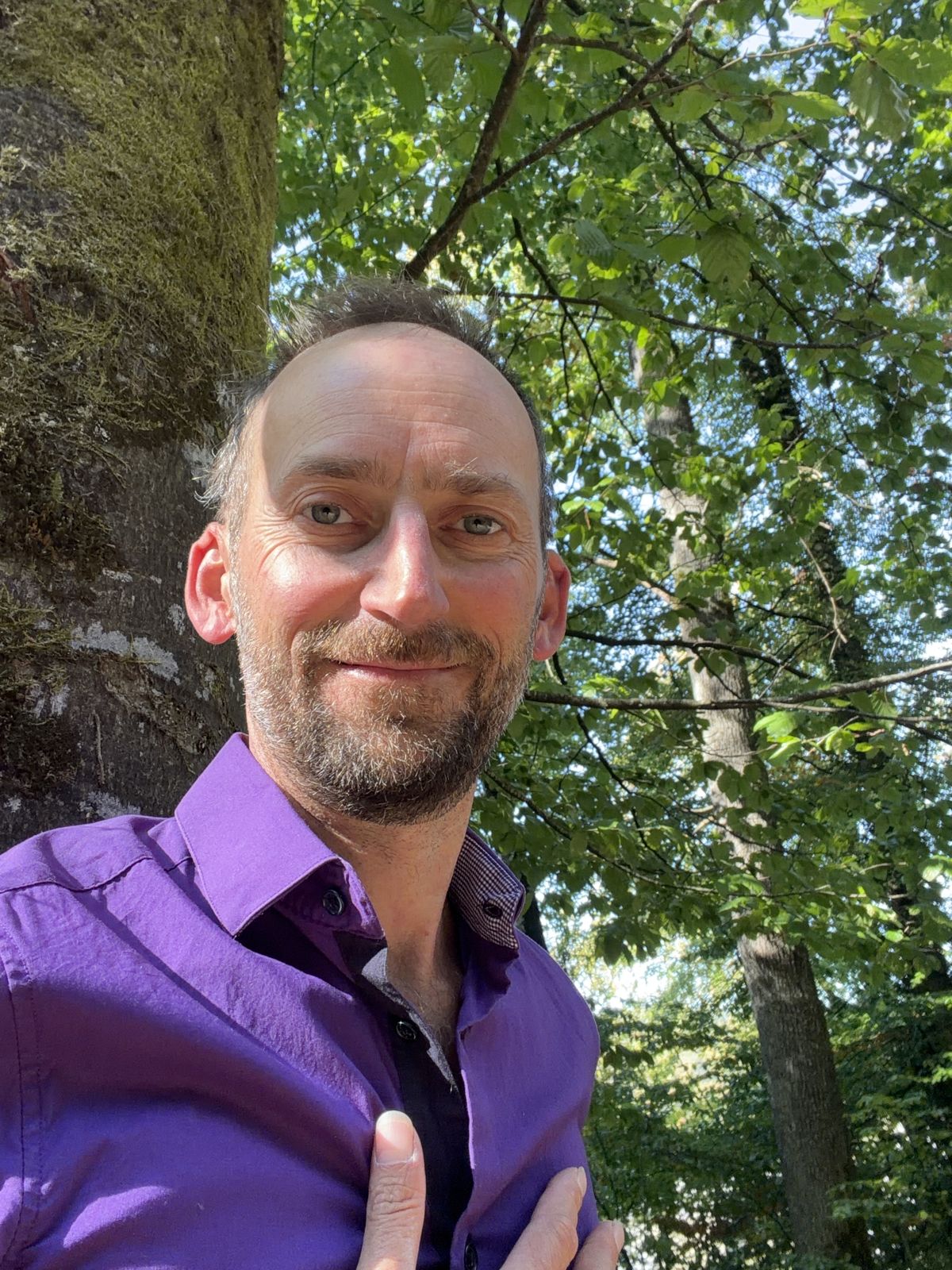 Noé Soleil im violetten Hemd, lächelnd im Wald